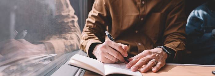 man-writing-in-notebook-on-train-1400x500